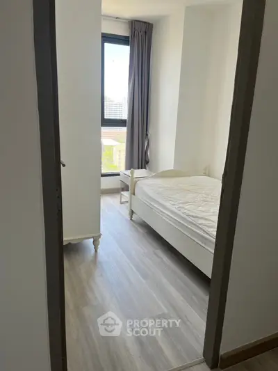 Cozy bedroom with wooden flooring and large window offering natural light.