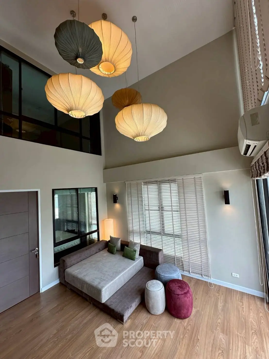 Spacious modern living room with high ceiling and stylish pendant lights, featuring a cozy sectional sofa and large windows.