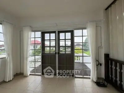 Bright living room with large windows and balcony access, offering a serene view of the neighborhood.