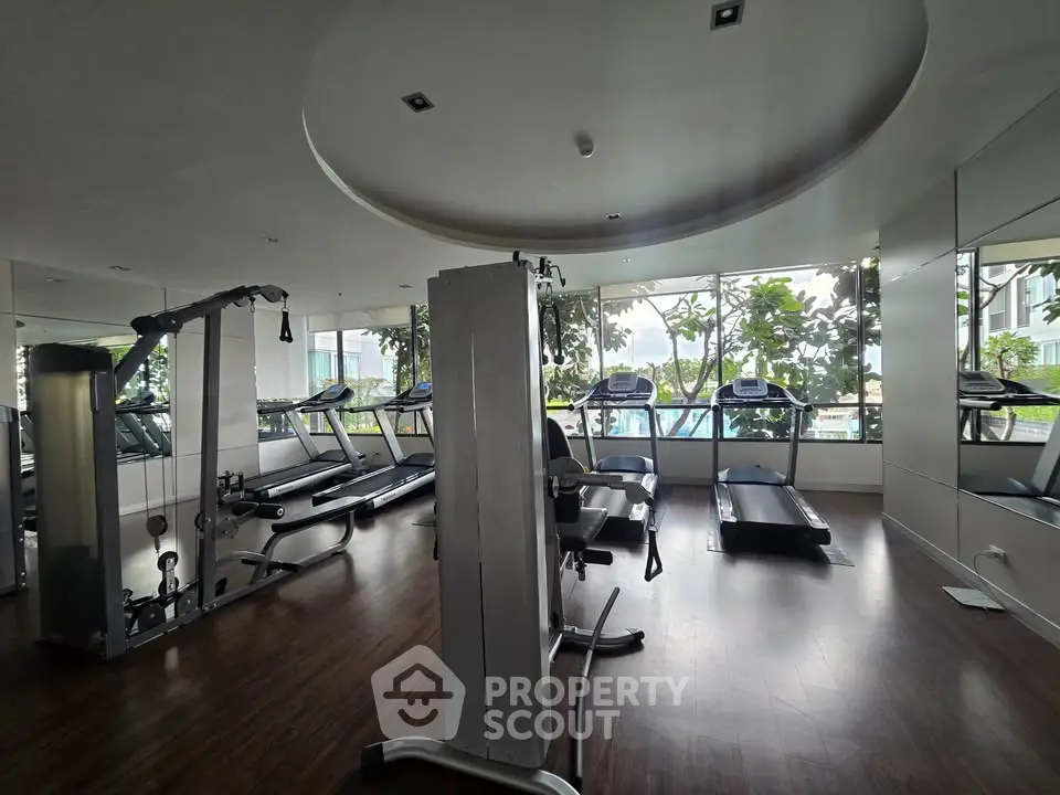 Spacious gym with modern equipment and large windows offering a lush garden view, perfect for fitness enthusiasts.