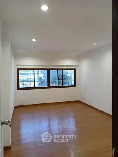 Spacious empty room with wooden flooring and large window, ideal for customization.