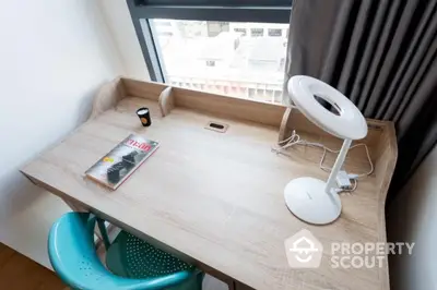 Modern study area with wooden desk, chair, and lamp by a window with city view.