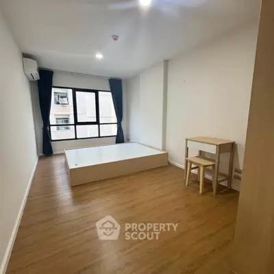 Spacious unfurnished bedroom with wooden flooring and large window in modern apartment.