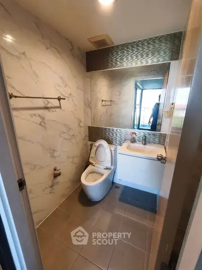 Modern bathroom with sleek design and large mirror, featuring elegant marble walls and contemporary fixtures.