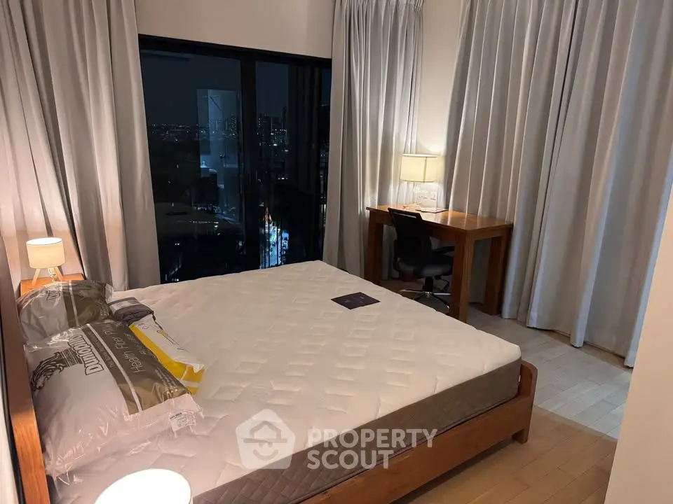 Modern bedroom with city view, featuring a cozy bed and a stylish work desk, perfect for urban living.