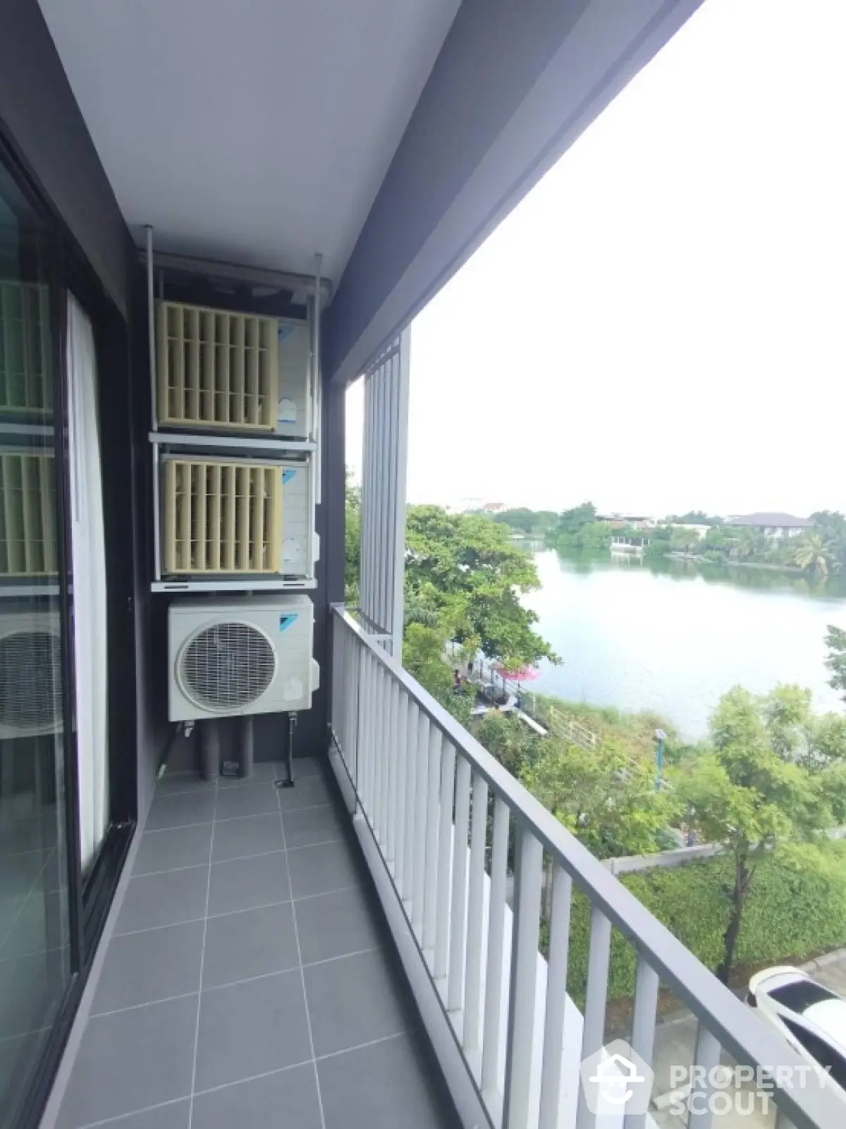 Spacious balcony with serene lake view and modern air conditioning units.