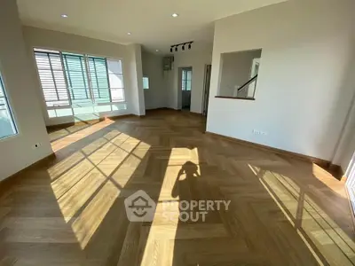 Spacious sunlit living room with elegant wooden flooring and large windows.