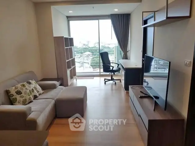 Modern living room with city view, featuring cozy sofa, TV, and work desk near large window.