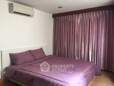 Cozy bedroom with purple bedding and curtains, featuring air conditioning and wooden flooring.