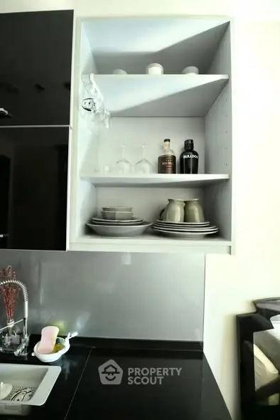 Modern kitchen with sleek black countertops and open shelving displaying glassware and dishes.