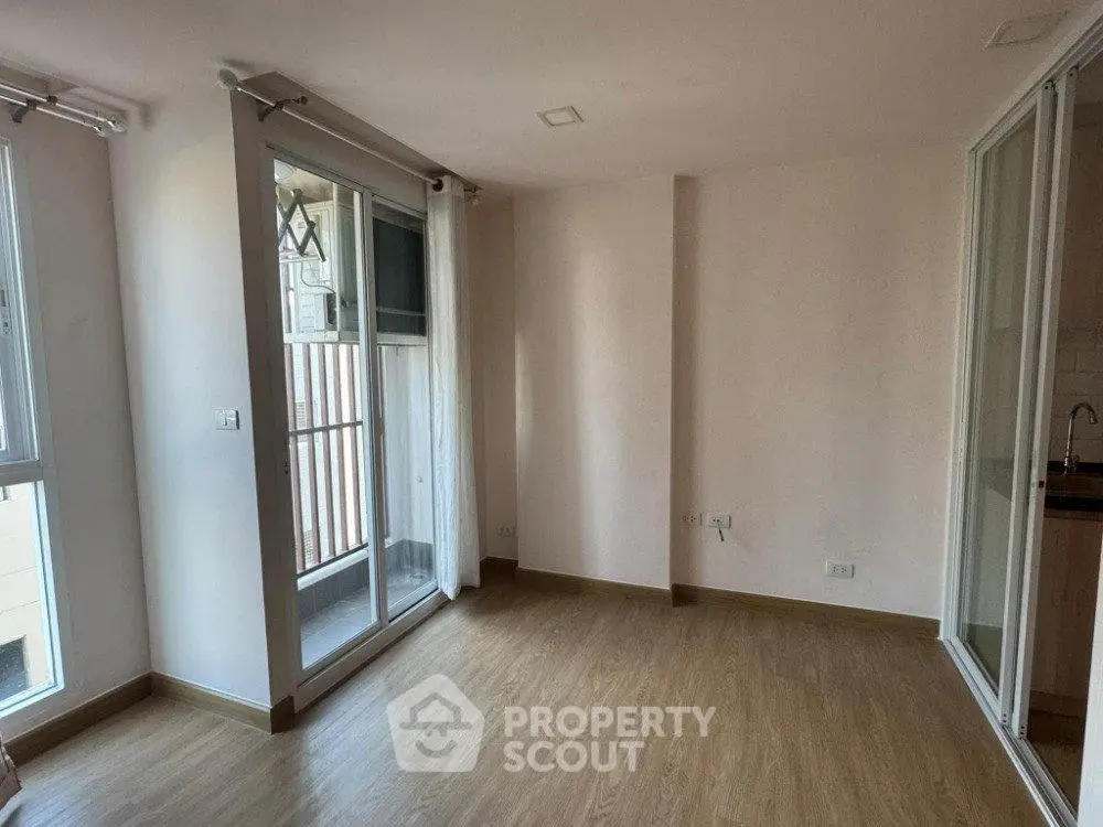 Spacious unfurnished room with wooden flooring and balcony access in modern apartment.