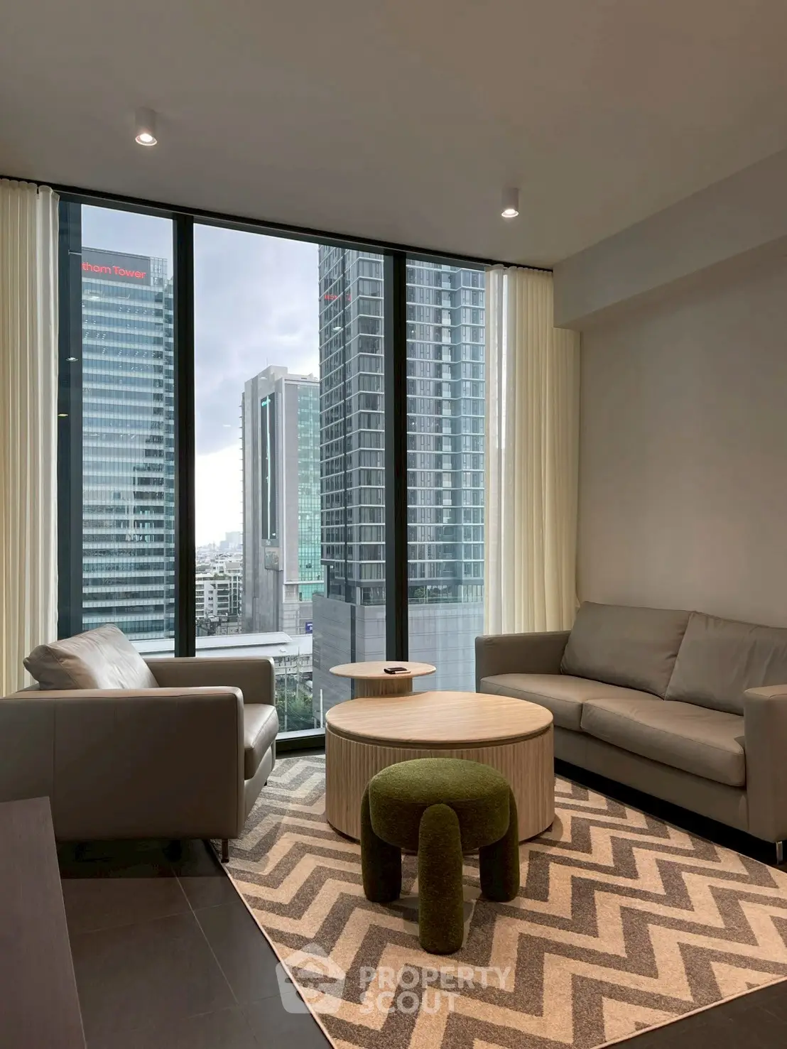 Modern living room with city view, featuring stylish furniture and large windows.