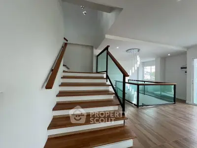 Modern staircase with wooden steps and glass railing in a bright, open interior space.