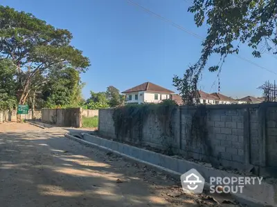 Expansive vacant land ready for development, surrounded by a secure wall and mature trees, near a serene residential area.