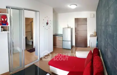 Modern living room with red sofa, wall clock, and open view to kitchen and bathroom.
