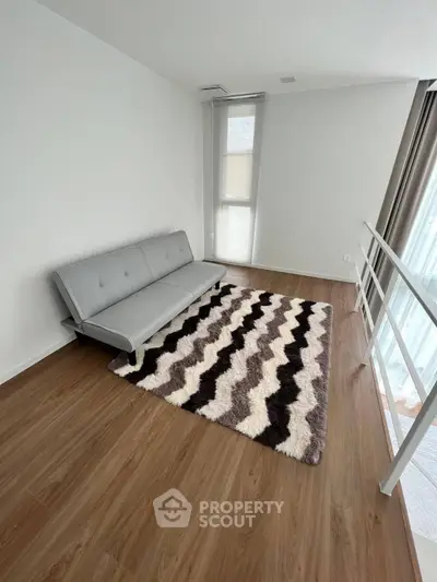 Minimalist living room with sleek grey sofa and stylish chevron rug, ample natural light, and pristine wooden flooring, perfect for modern living.