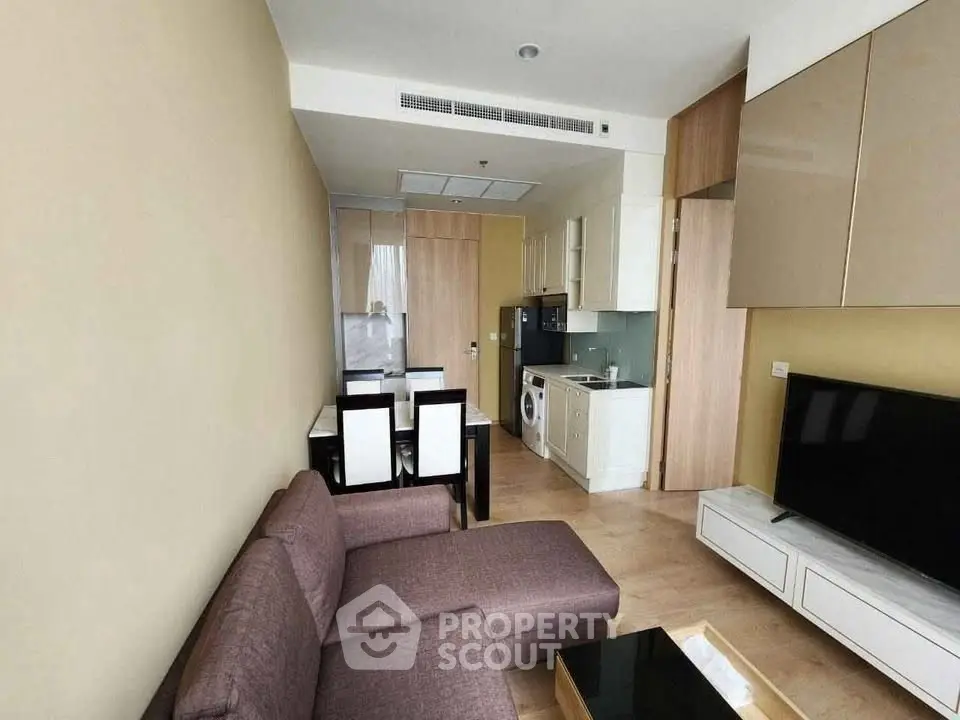 Modern living room with open kitchen and dining area, featuring sleek furniture and appliances.
