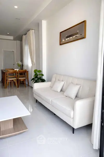 Modern living room with elegant white sofa and dining area, featuring sleek decor and natural light.