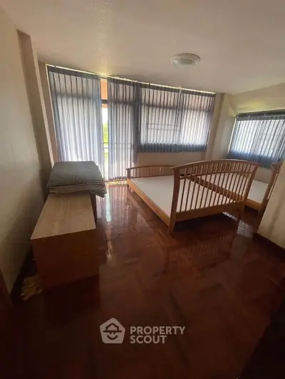 Spacious bedroom with wooden flooring and large windows for natural light.