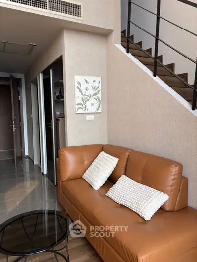 Modern duplex living room with stylish brown leather sofa and elegant staircase.