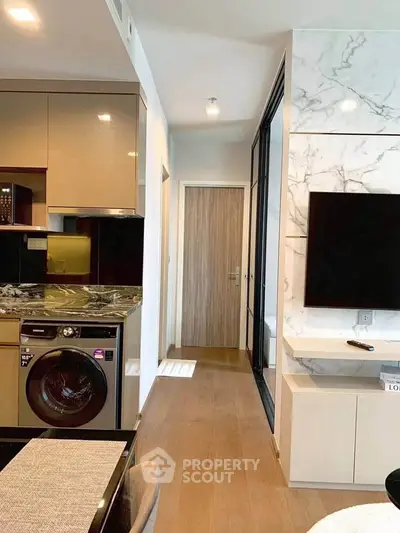 Modern apartment interior with sleek kitchen and stylish living area featuring a washing machine and wall-mounted TV.
