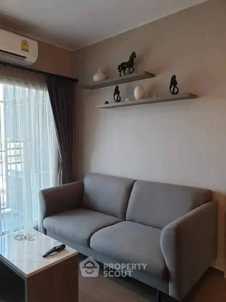 Modern living room with gray sofa and decorative shelves, featuring natural light from large windows.