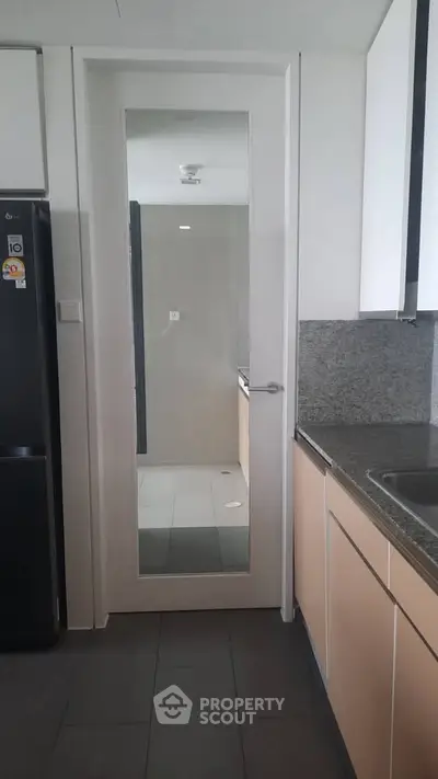 Modern kitchen with sleek cabinetry and granite countertops, featuring a mirrored door and stainless steel appliances.
