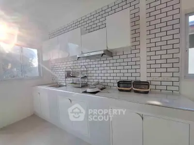 Modern kitchen with sleek white cabinets and subway tile backsplash, flooded with natural light from large windows.