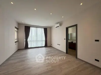 Spacious empty room with large window and wooden flooring, ideal for customization.