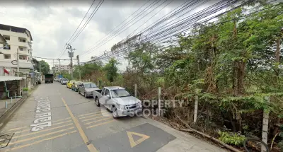 Urban street view with parked cars and greenery, potential real estate development area.