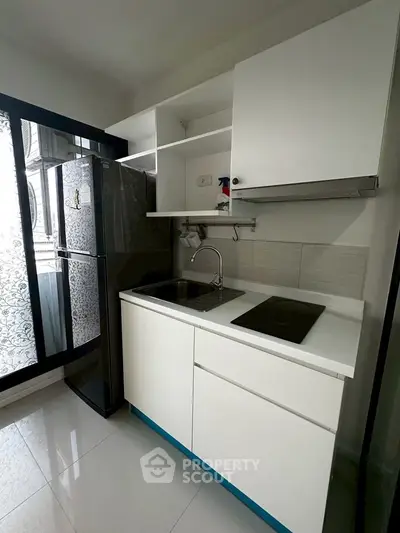 Modern kitchen with sleek cabinetry, induction cooktop, and large fridge in a bright, compact space.