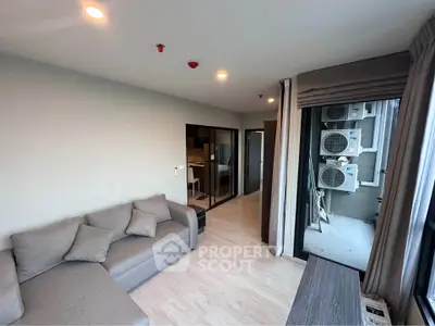 Modern living room with cozy gray sofa and large windows overlooking air conditioning units.