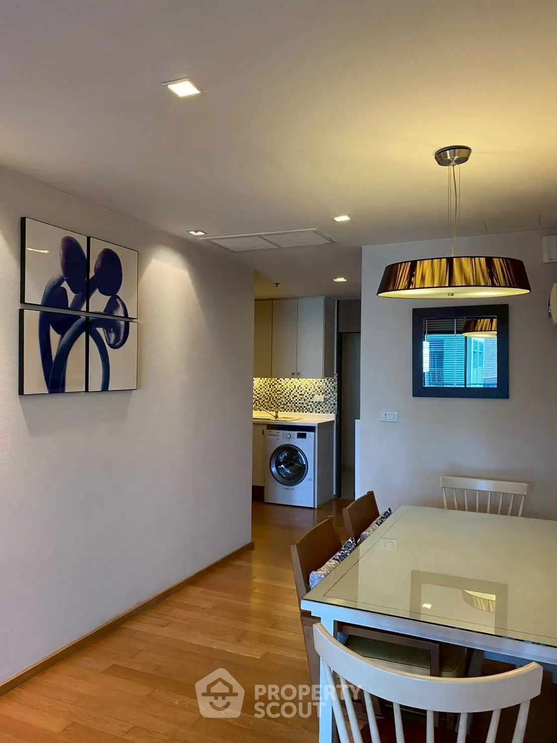 Modern dining area with stylish lighting and open view to kitchen with washing machine.