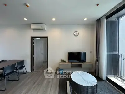 Modern living room with sleek furniture and balcony access, featuring a wall-mounted TV and stylish decor.