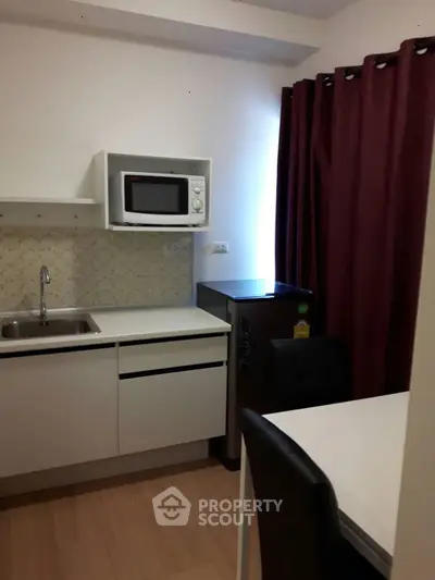 Compact kitchen with microwave, fridge, and dining area in modern apartment.