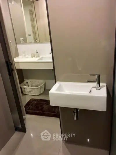 Modern bathroom with sleek fixtures and minimalist design, featuring a small sink and a large mirror.