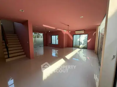 Spacious modern living room with pink walls, large windows, and sleek staircase.