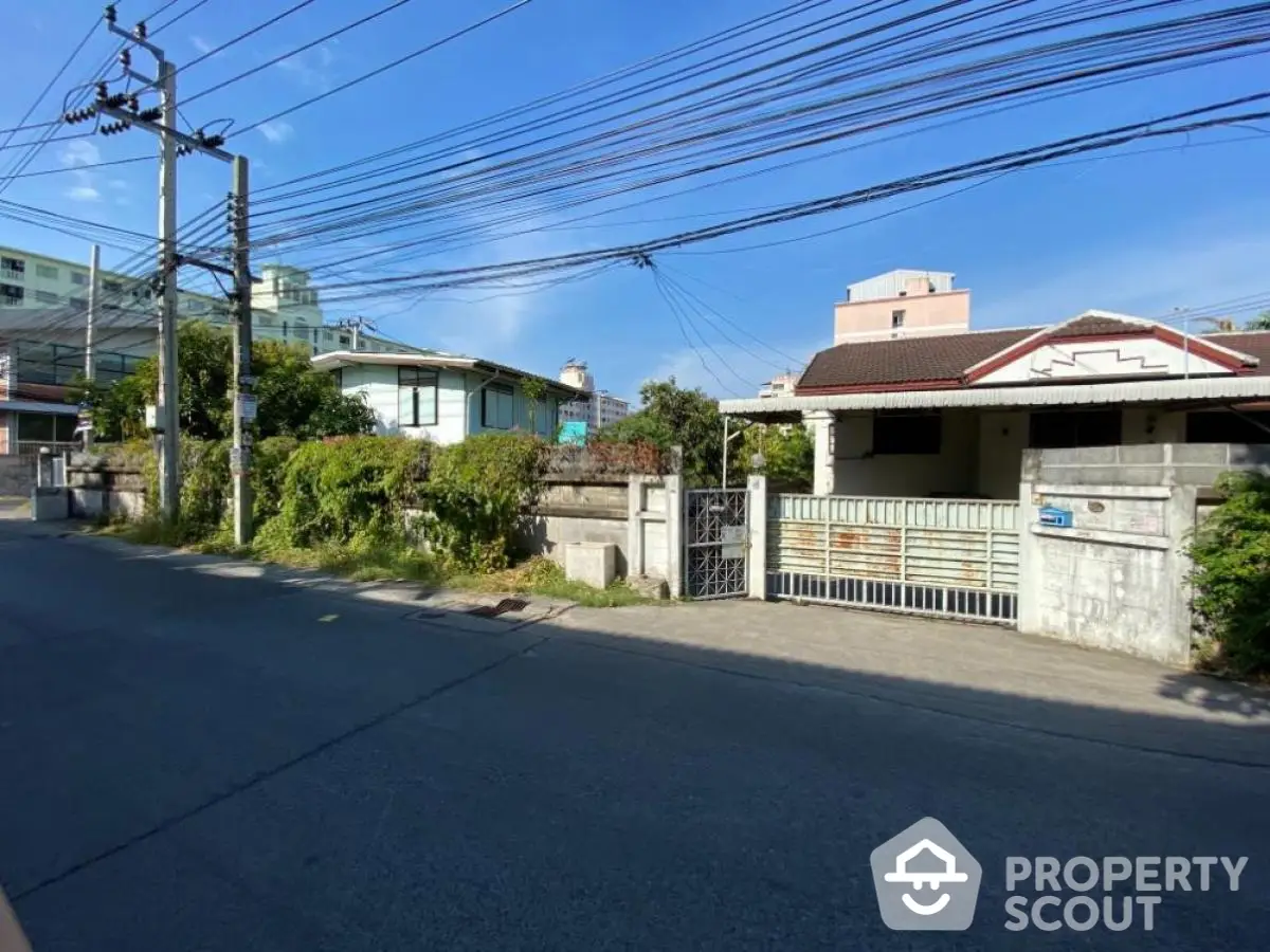 Charming suburban house with gated entrance and lush greenery on a sunny day.