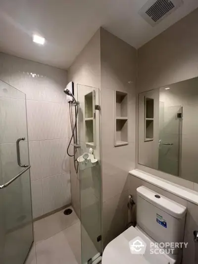 Modern bathroom with sleek glass shower enclosure, built-in shelving, and premium fixtures, offering a clean and functional space.