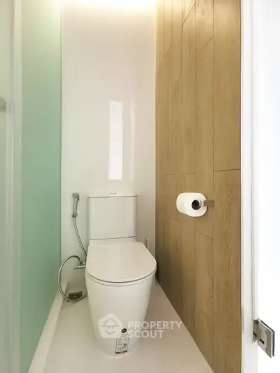 Modern compact bathroom with sleek toilet and wood panel accent wall.
