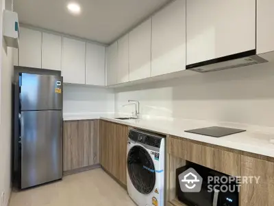 Modern kitchen with sleek cabinets, washing machine, and stainless steel fridge in a compact layout.