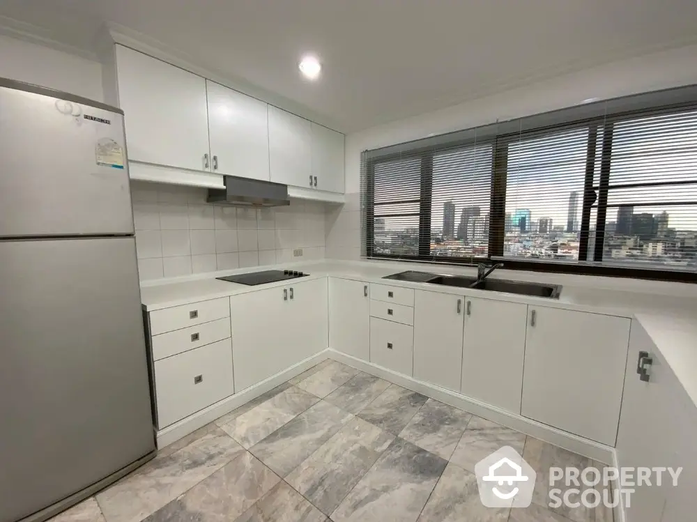 Modern kitchen with city view, featuring sleek white cabinets and stainless steel appliances.