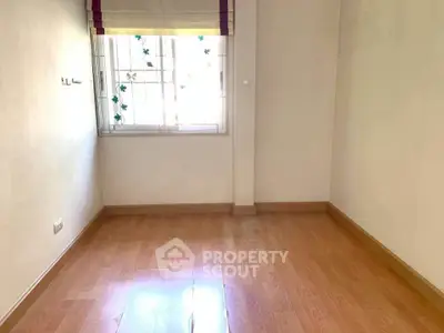 Spacious empty room with wooden flooring and natural light through window.