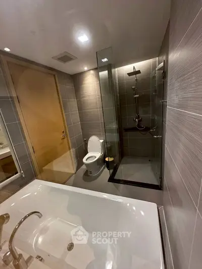 Modern bathroom with glass shower, bathtub, and sleek fixtures in luxury apartment.