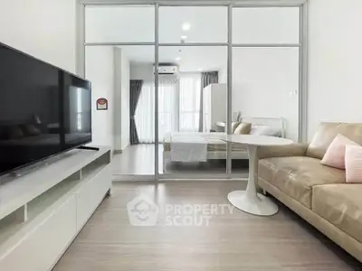 Modern living room with sleek furniture and glass partition leading to a bright bedroom.