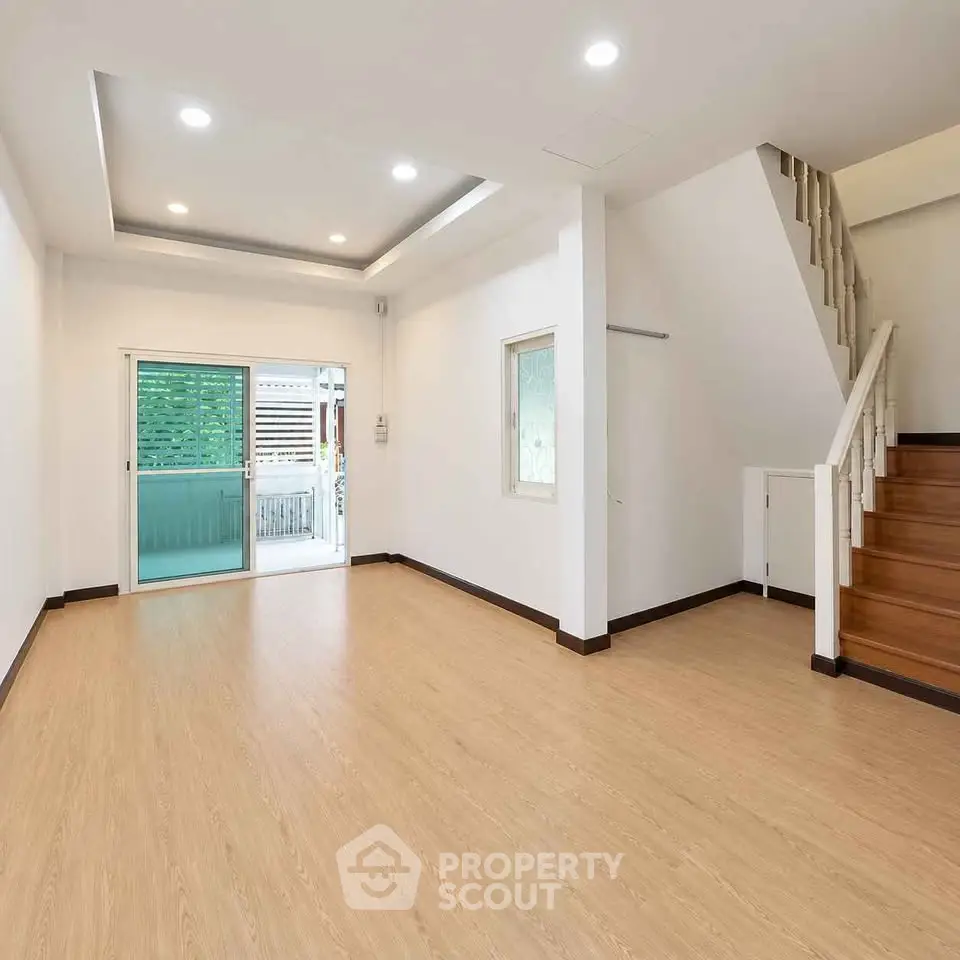 Spacious modern living room with wooden flooring and staircase, featuring sliding glass doors to a balcony.