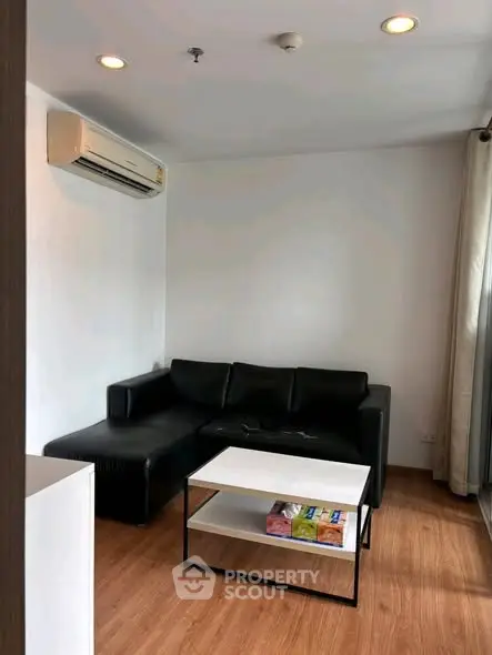 Modern living room with black leather sofa and sleek coffee table in a cozy apartment setting.