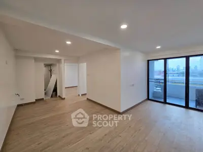 Spacious modern living room with balcony and city view, featuring sleek wooden flooring.
