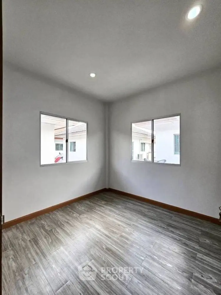 Bright empty room with wooden flooring and two windows, ideal for customization.