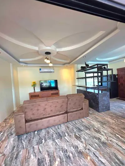 Spacious living room with elegant ceiling design and marble flooring, featuring a cozy sofa and modern entertainment setup.